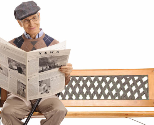 Full length shot of a senior man reading a newspaper on a bench isolated on white background