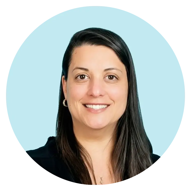 A woman with straight dark hair, wearing a black top and small hoop earrings, smiles at the camera against a light blue background.
