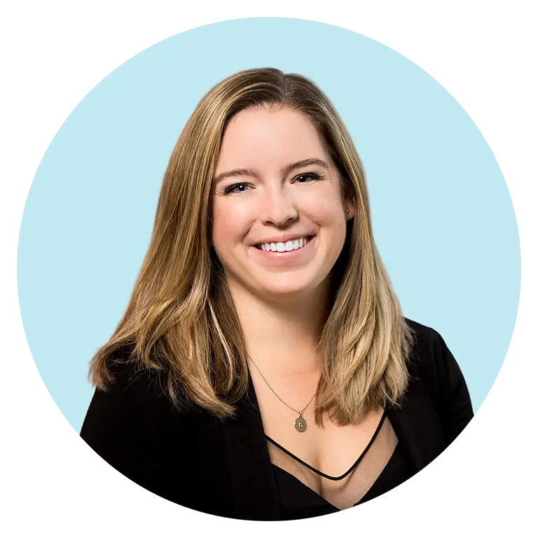 A woman with straight, shoulder-length blonde hair, wearing a black top and necklace, smiles in front of a light blue background.