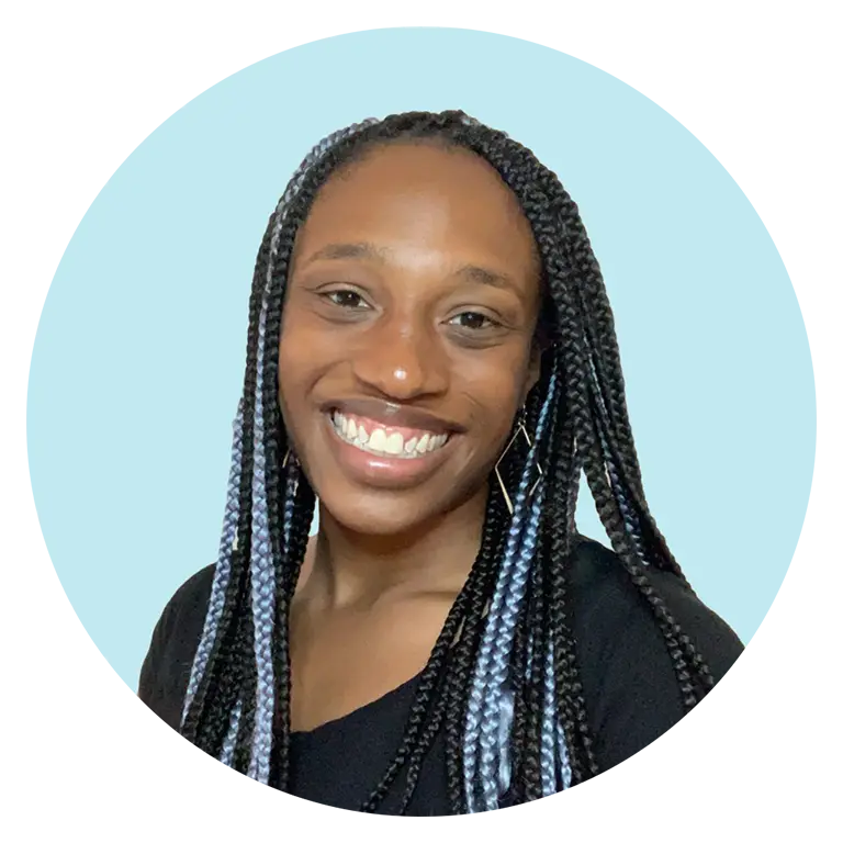 A person with long box braids, wearing a black top, smiles in front of a light blue background.
