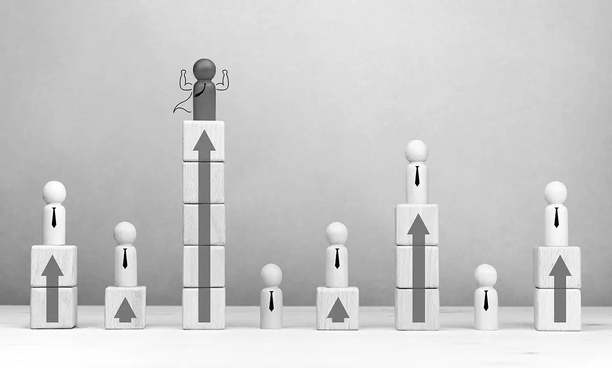 Seven wooden figures stand on block columns of varying heights, each topped with an arrow, suggesting progression or career advancement; one figure stands highest with raised arms.