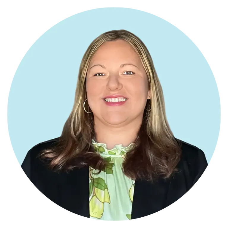 A woman with straight, light brown hair wearing a light green patterned blouse and black jacket, smiling against a light blue background.