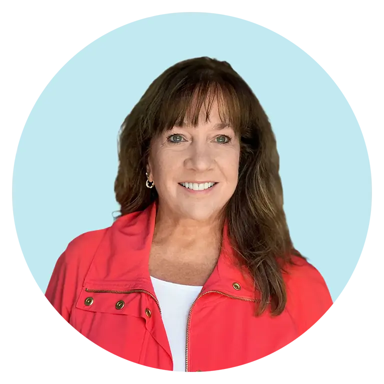 Woman with long brown hair wearing a red jacket over a white top, smiling in front of a light blue background.