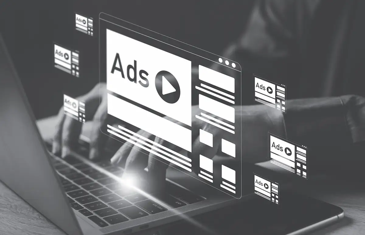Person typing on a laptop with digital illustrations of online ads and a play button superimposed on the screen, representing online advertising.