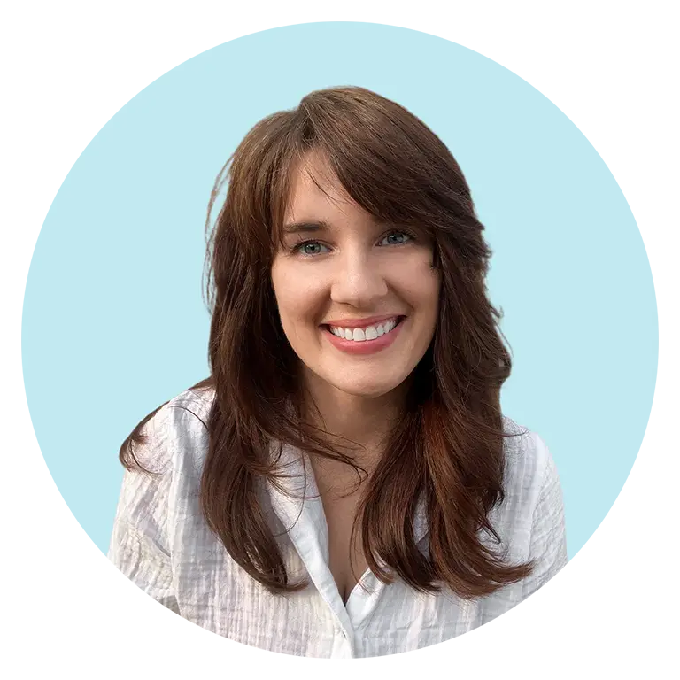A woman with long brown hair and a white shirt smiles at the camera against a light blue background.