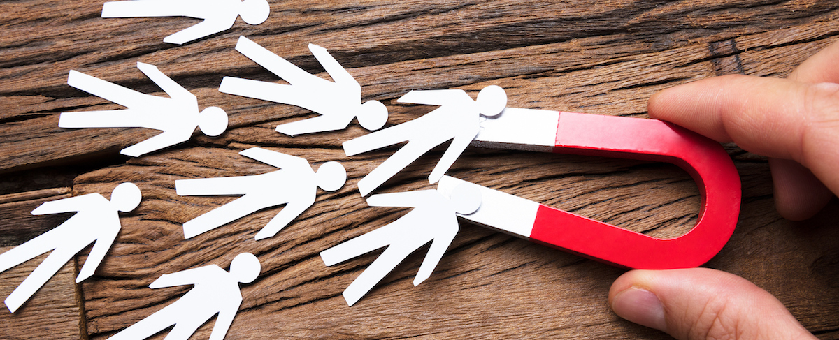 A hand holds a red horseshoe magnet, attracting paper cutout figures of people on a wooden surface, symbolizing how a senior living lead generation agency draws in potential residents.
