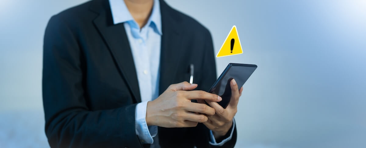 A person in a business suit uses a smartphone, with a yellow warning triangle containing an exclamation mark beside the device—highlighting the importance of caution in senior living branding communications.