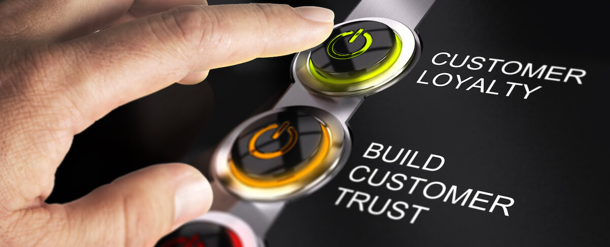 A hand presses a green power button labeled "Customer Loyalty" above an orange button labeled "Build Customer Trust," highlighting the interplay of Loyalty vs. Trust in fostering strong customer relationships.