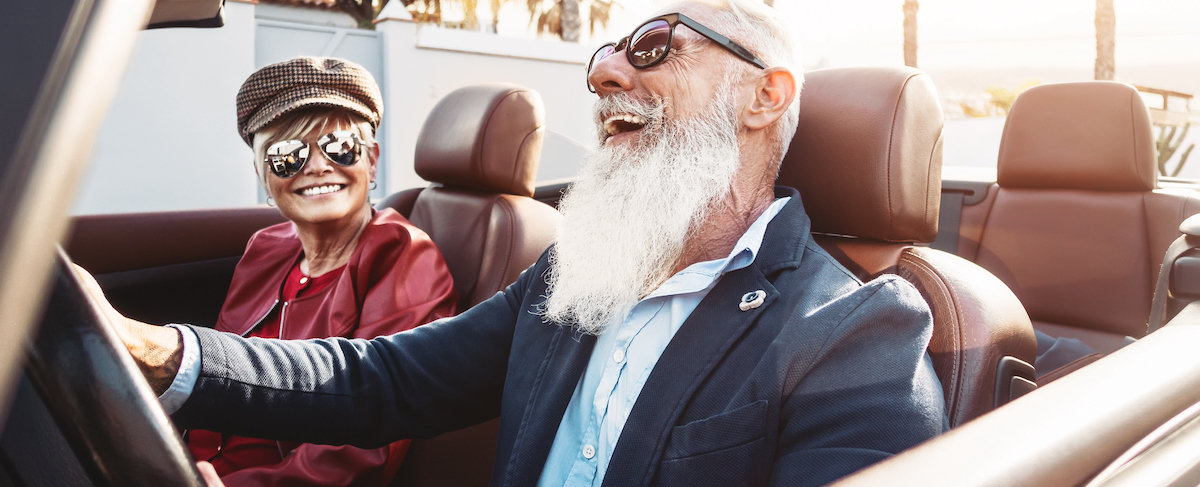 Two older adults wearing sunglasses and stylish clothes sit in a convertible car, smiling and enjoying a sunny day—a perfect image for independent living marketing ideas.