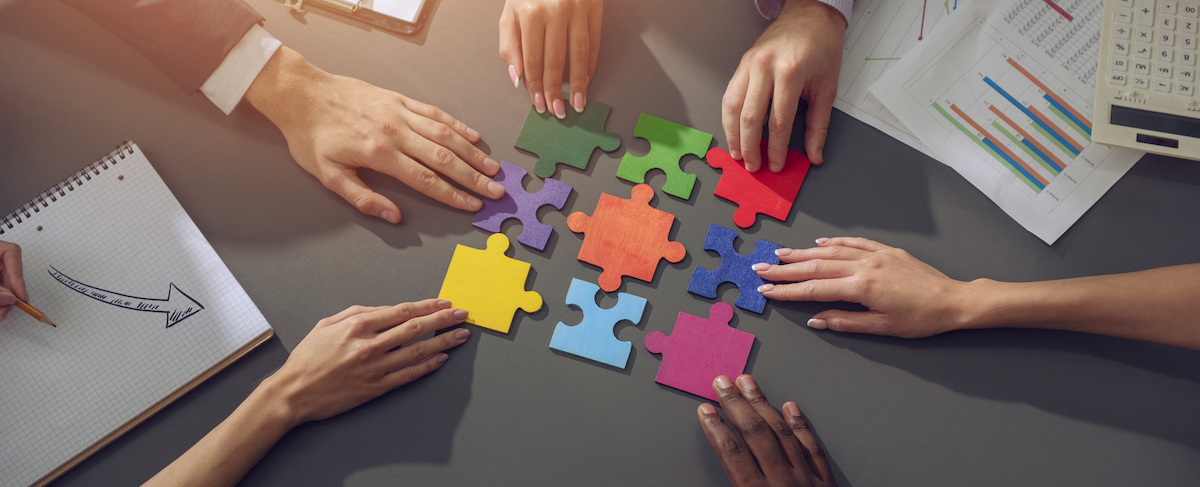 Several hands assemble colorful puzzle pieces on a table surrounded by business documents, illustrating teamwork and strategy—much like what is an integrated marketing campaign in action.