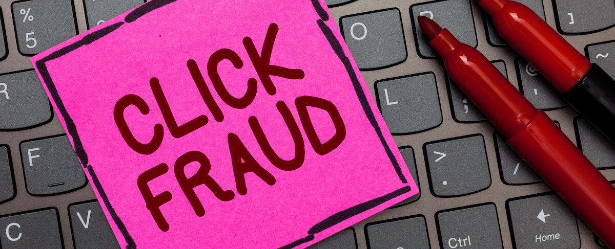 A sticky note with "CLICK FRAUD" written on it is placed on a computer keyboard next to two red markers, highlighting concerns about ad fraud in online campaigns.