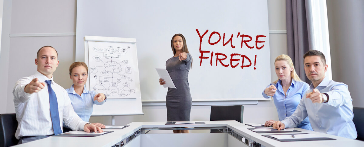 A woman stands by a whiteboard with "You're Fired!" written on it, while four seated people in business attire from a Senior Living Marketing Agency point toward the camera.
