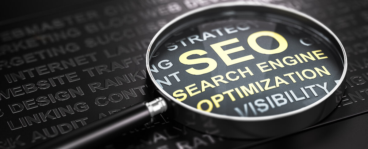 A magnifying glass highlights the words "SEO Search Engine Optimization" on a dark background, with related terms embossed in the surface—perfect for a Senior Living SEO Company focused on boosting online visibility.