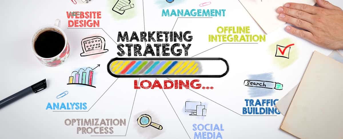 A hand at a desk with a coffee cup, notebook, and a diagram showing elements—like website design, management, and analytics—surrounding a loading bar, illustrating how to market senior living communities effectively.