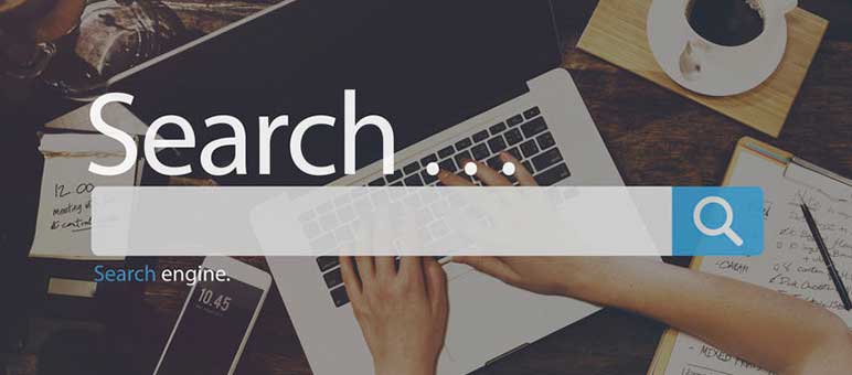 Person typing on a laptop with a large search bar graphic overlay, various office supplies on the desk, highlighting the importance of senior living SEO in optimizing search results.