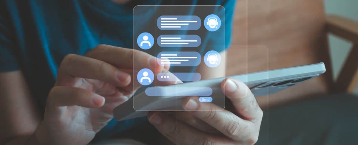A person using a smartphone with illustrated chat bubbles appearing above the screen, suggesting online messaging or virtual conversation with a chatbot.