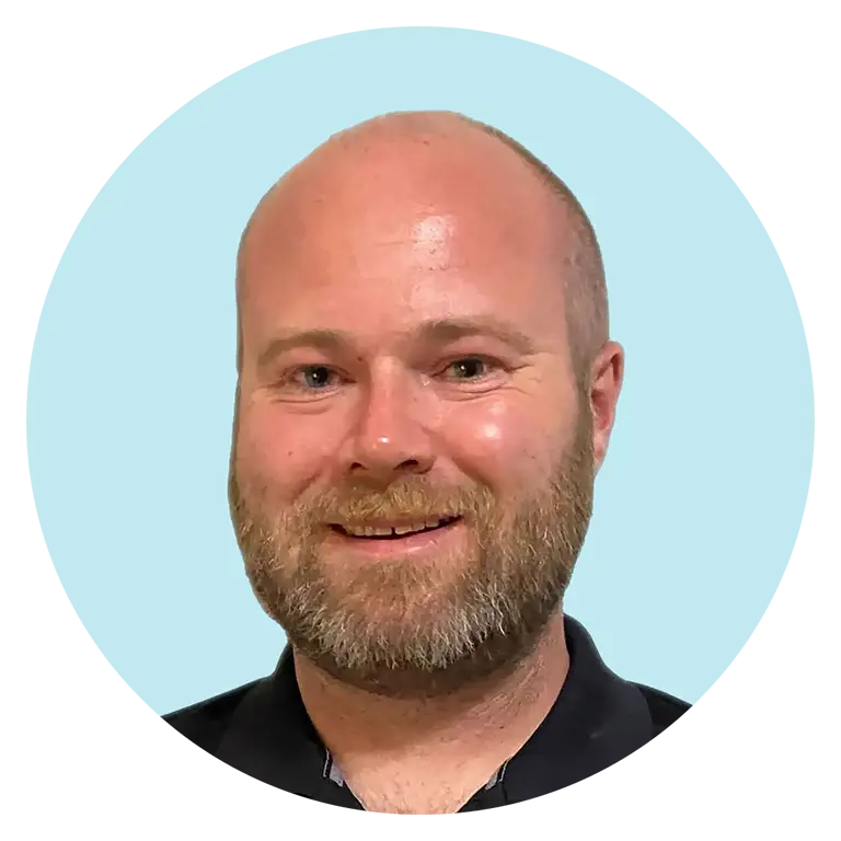 A smiling bald man with a beard wearing a black shirt, shown against a light blue background with a rounded border.