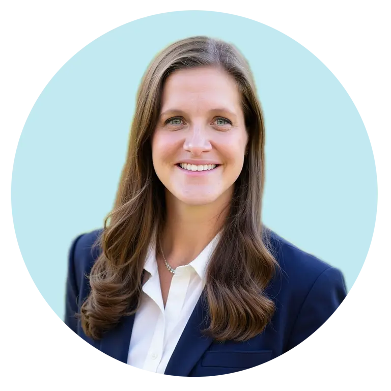 A woman with long brown hair wearing a navy blazer and white shirt, smiling at the camera against a light blue background.