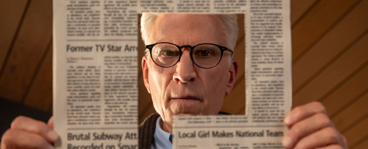 A man with glasses looks through a square hole cut in the center of a newspaper, as if searching for creative marketing memory care ideas, holding it up in front of his face.