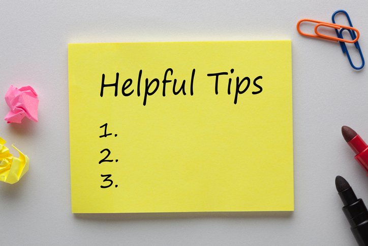 A yellow sticky note labeled "Helpful Tips" with a numbered list from 1 to 3, surrounded by crumpled paper, paper clips, and two lipsticks on a gray surface—perfect for quick information management ideas.