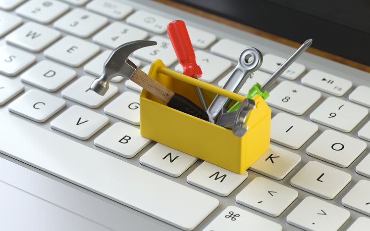 A small yellow toolbox filled with miniature sales tools sits on a computer keyboard.