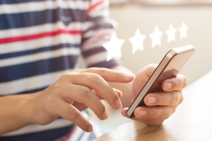 A person holding a smartphone with five floating stars above the screen, illustrating the impact of senior living reputation management and positive reviews.