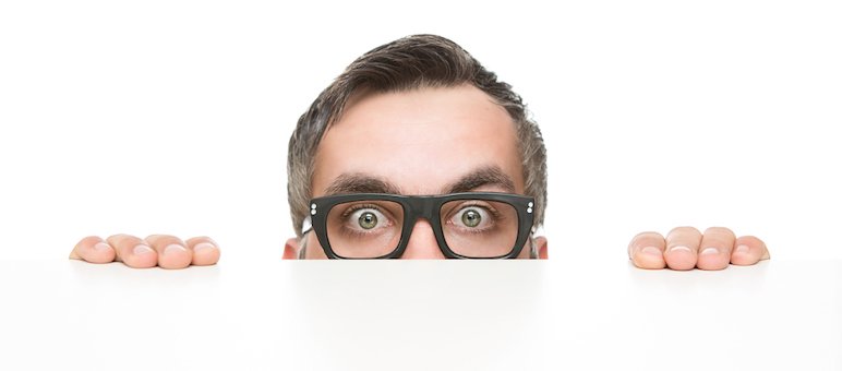 A person wearing black glasses looks over a white surface, as if conducting competitor analysis, with only their eyes, forehead, and hands visible against a plain white background.