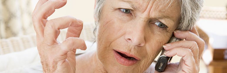Older woman with gray hair holding a phone to her ear, looking concerned and raising her hand in a questioning gesture—perhaps she’s asking about senior living sales options.