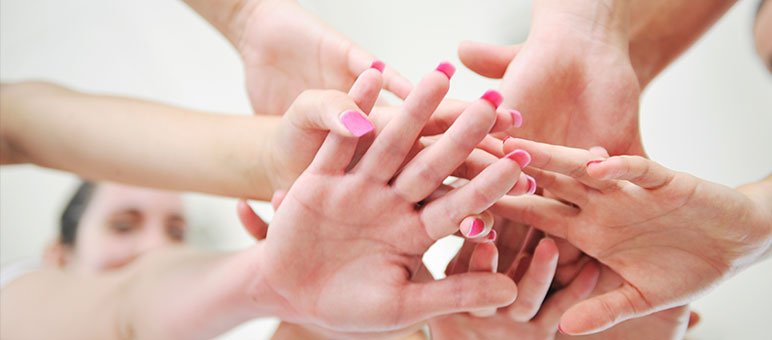 Several hands with pink fingernails are stacked together in a gesture of teamwork or unity, reflecting the collaborative spirit essential in senior living sales, set against a softly blurred background.
